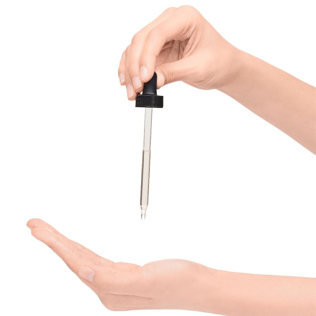 Mujer aplicando aceite corporal anti estrías con gotero en la palma de su mano.